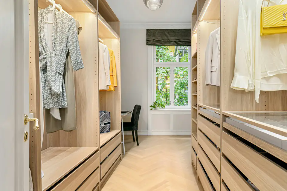 Oak walk-in wardrobe with open shelving and a window at the far end, a storage idea for homes in Newcastle